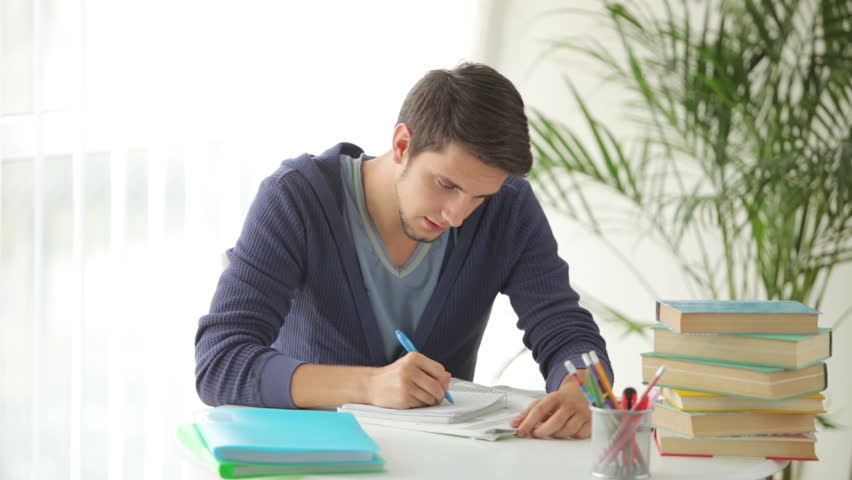 Young man sitting at table and writing in notebook