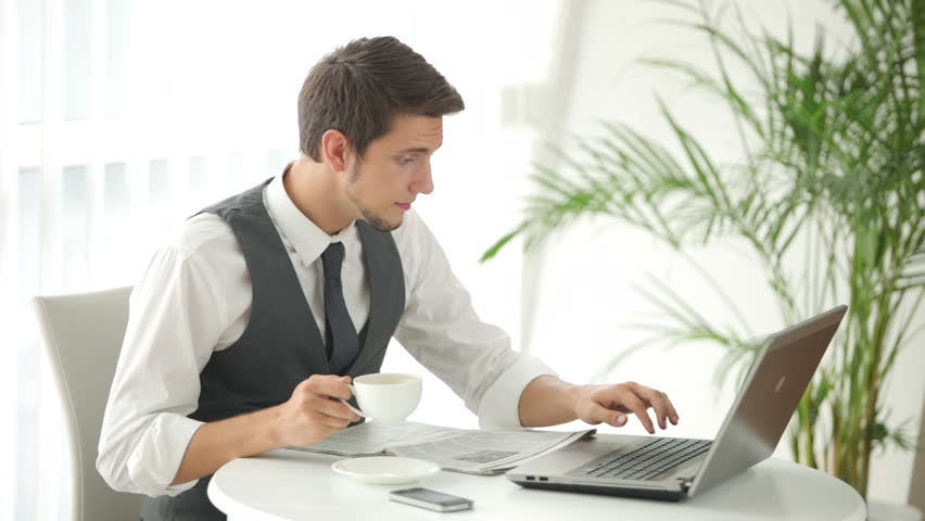 Young man sitting at table using laptop and drinking coffee