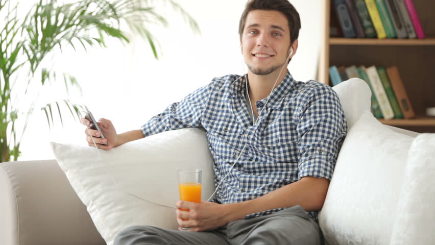 Good-looking guy sitting on sofa and listening to music with earphones