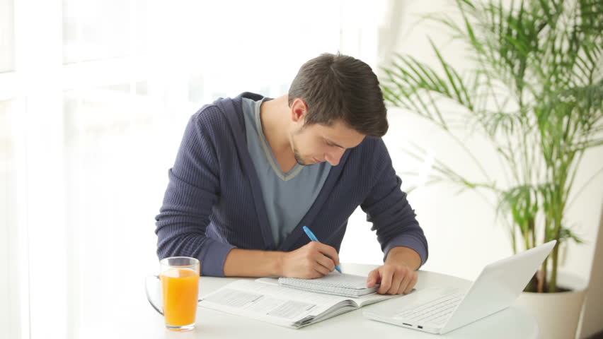 Young man sitting at table and studying with laptop and books