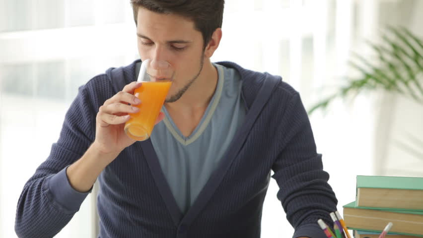 Charming young man sitting at table studying and drinking juice
