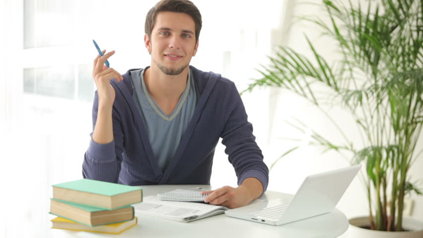 Young man sitting at table studying with books and laptop