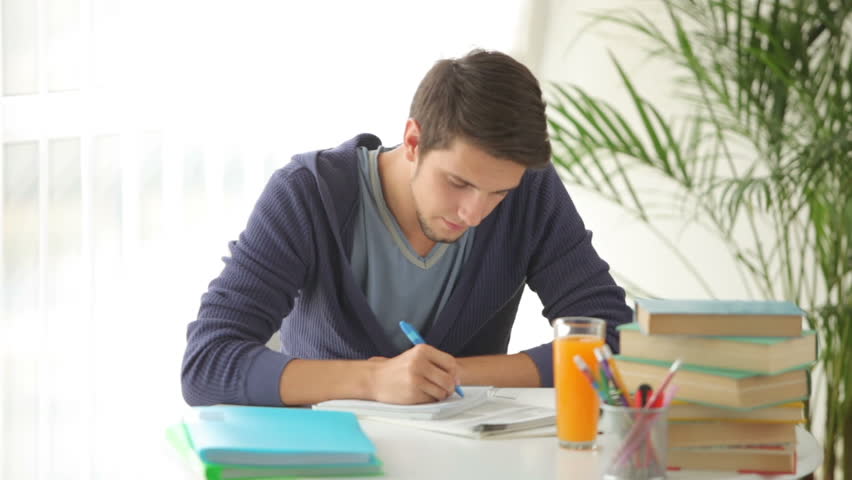 Young man sitting at table studying and writing in notebook