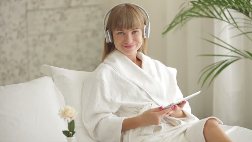 Happy young woman in headset sitting on bed and using touchpad