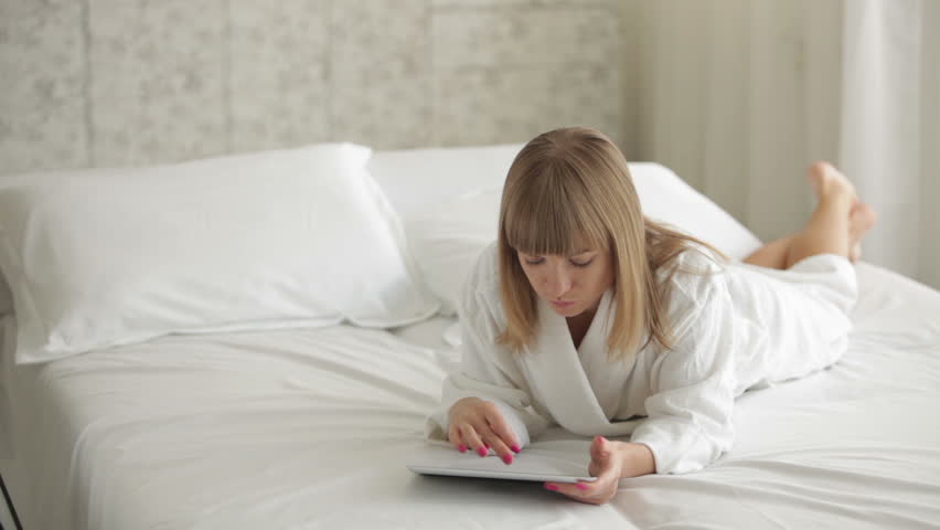 Pretty young woman relaxing on bed using touchpad and smiling