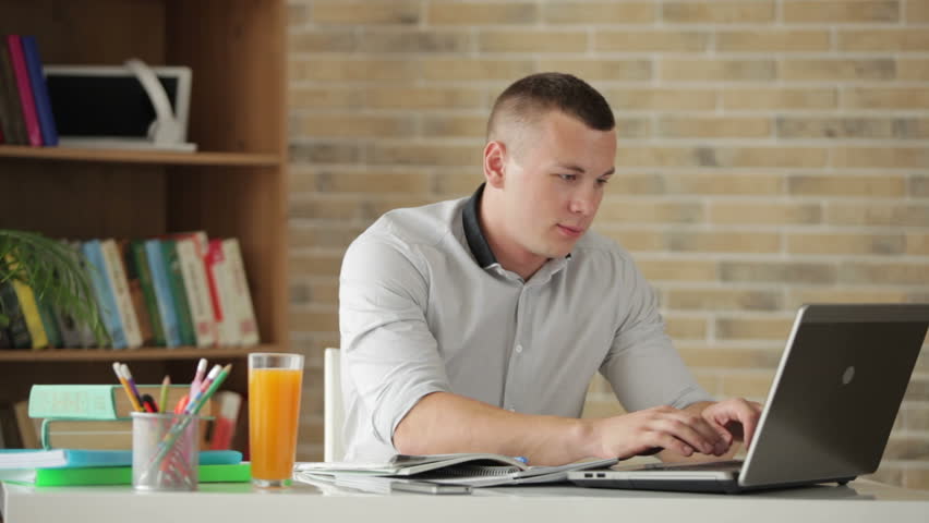 Attractive male student sitting at table and studying with books and laptop