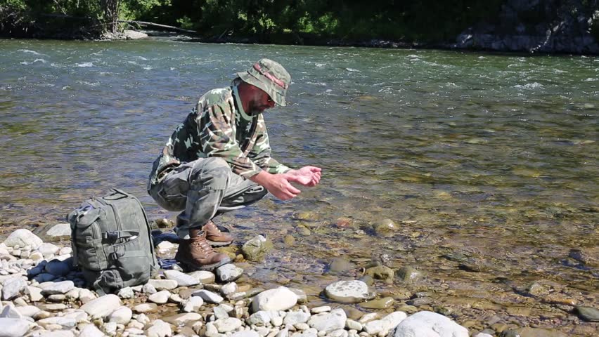 Hiker drinking water from the river in the hands of a hot day.