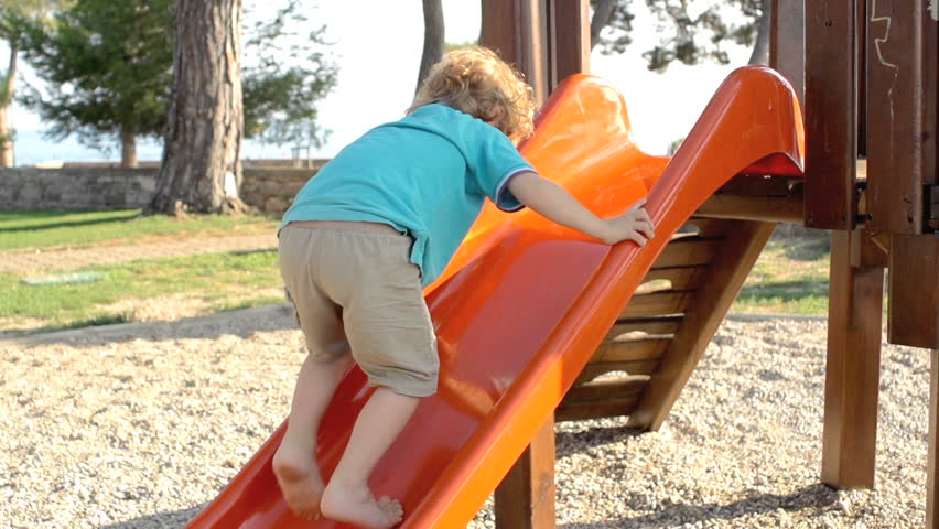 Slow Motion Shot Of A Little Red-Haired Boy Climbing Up A Slide Outdoors In The