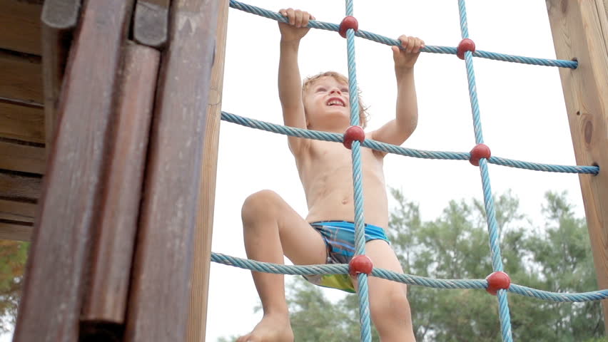Slow Motion Of A Cute Boy Climbing Up A Rope Ladder Outdoors On The Playground.