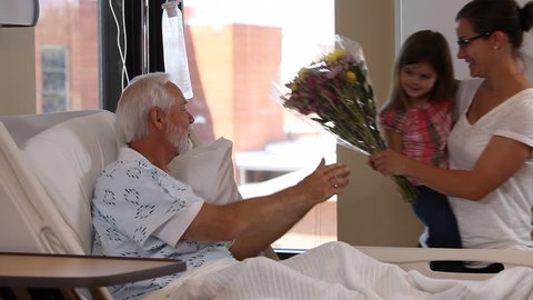 Woman and young girl visit senior man in hospital