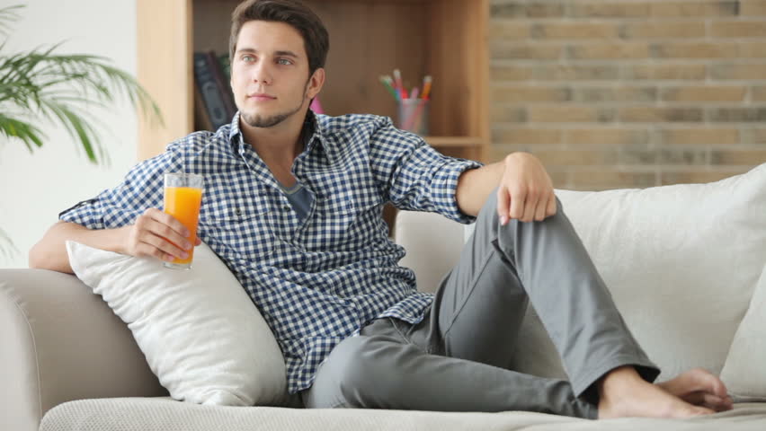 Good-looking guy sitting on couch and drinking juice