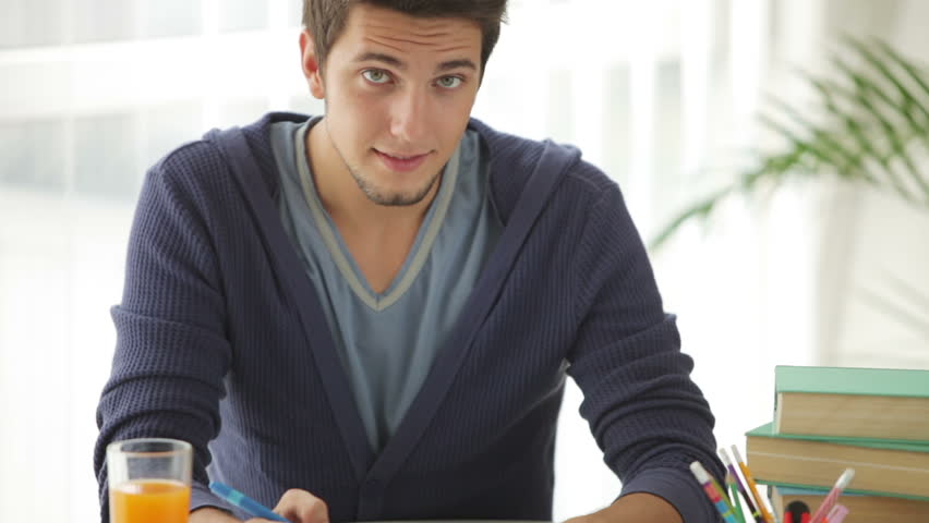Cute guy sitting at table studying and writing in notebook