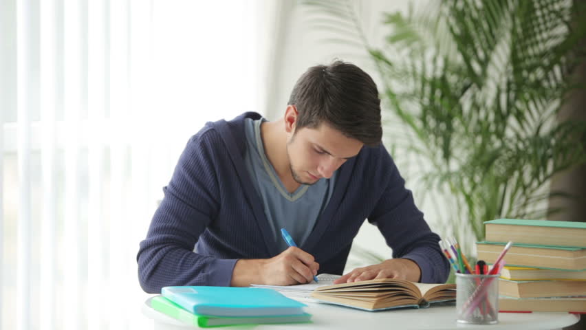 Handsome guy sitting at table studying and writing in notebook