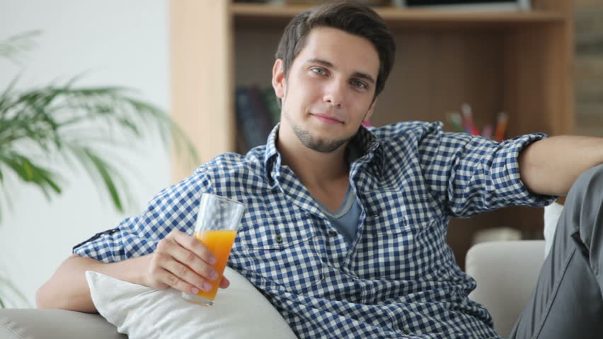 Handsome guy relaxing on sofa drinking juice and smiling