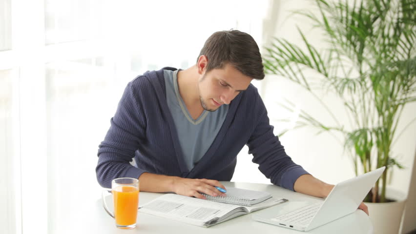 Good-looking young man studying at table with books and laptop