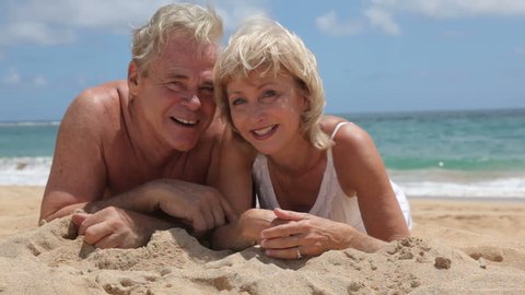 Portrait of senior couple laying in sand at beach