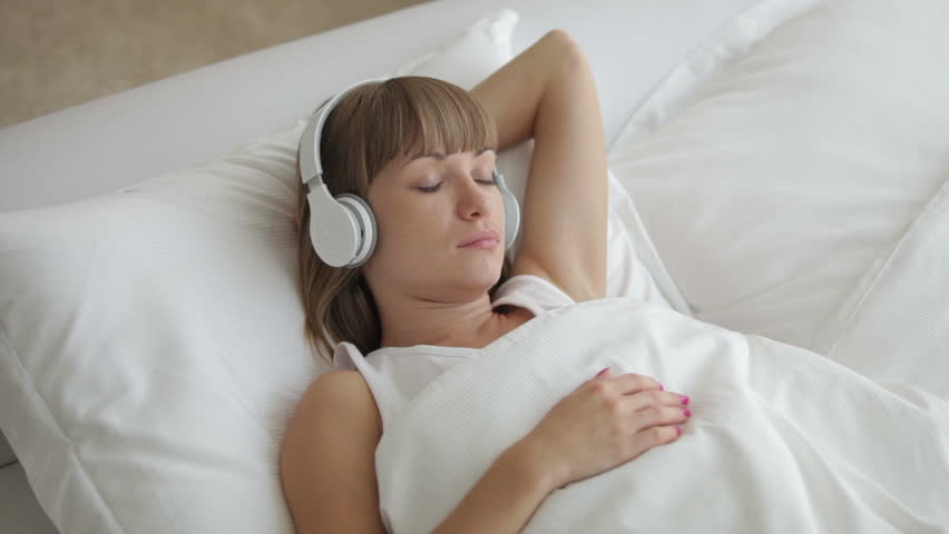 Young woman relaxing in bed and listening to music with headphones