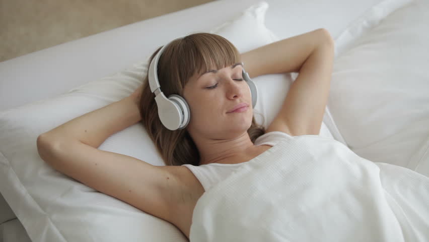 Young woman in headphones lying in bed and smiling