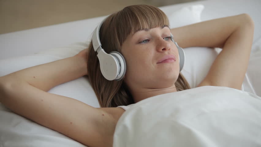 Young woman in headset relaxing in bed and smiling