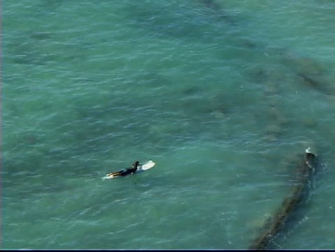 Surfer paddling out across reef and submerged break wall.
