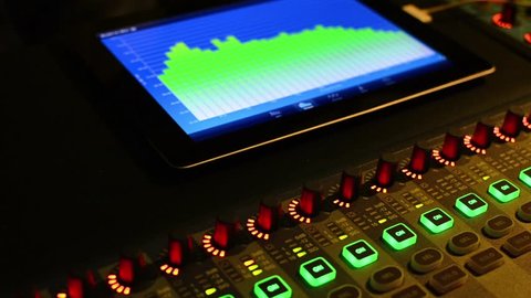 Music studio audio mixer with digital VU meter display showing audio waves.