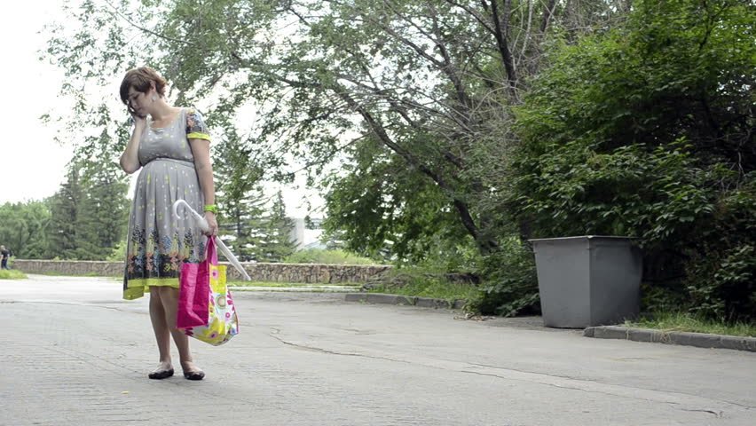 Young pregnant woman is walking in a park talking on the phone