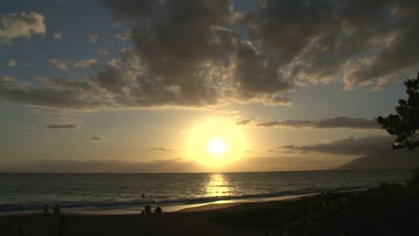 People relaxing on beach with sun setting in Maui, Hawaii.