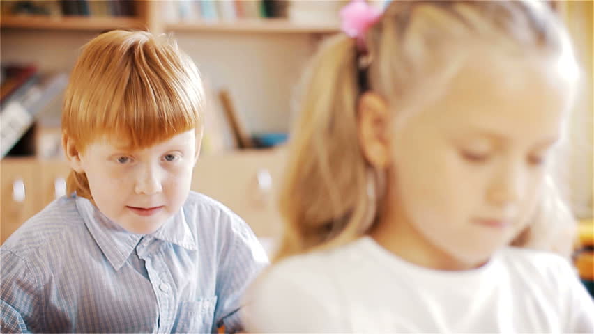 Little redhead schoolboy pulling girl's plait during lesson. Teasing children. 