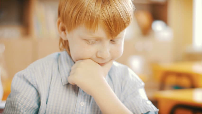 Little redhead schoolboy sitting behind desk during lesson in school