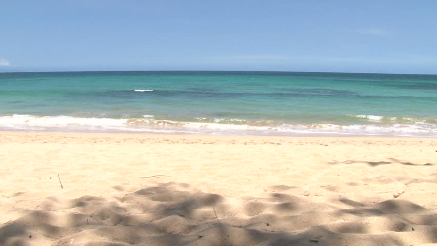 Waves crashing gently on quiet sandy beach in Maui, Hawaii, camera tilt down.