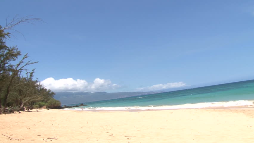 Waves crashing gently on quiet sandy beach in Maui, Hawaii.