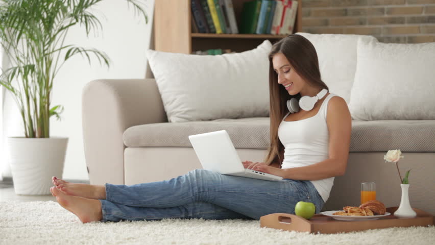 Cute girl in headset sitting on floor and using laptop