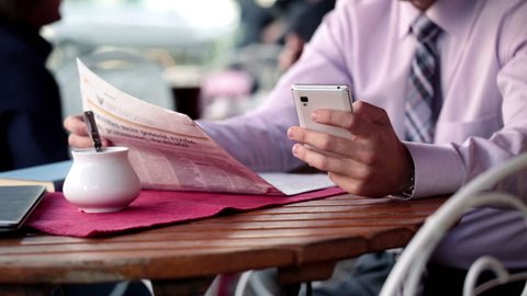 Young businessman with smartphone and newspaper in cafe
