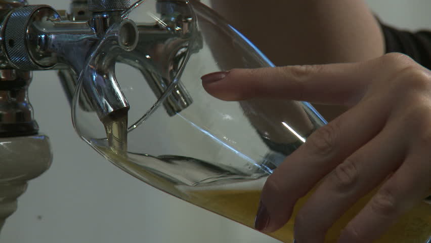 Close up on beer being poured from a tap. Small flies hover around in parts of