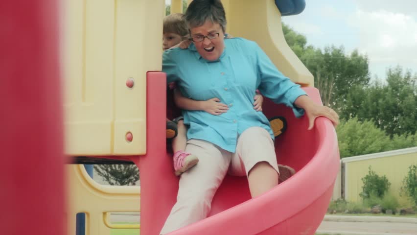 A grandma going down a slide with her grandchildren at the park