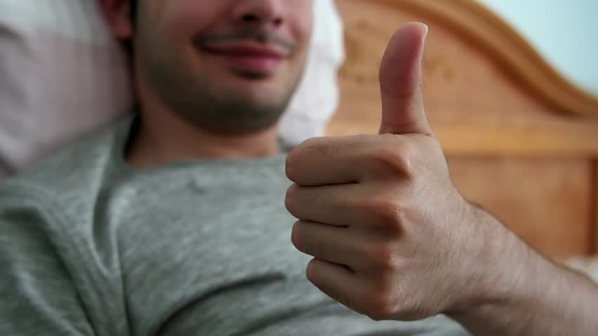 Young man gives thumbs up while he's in bed.