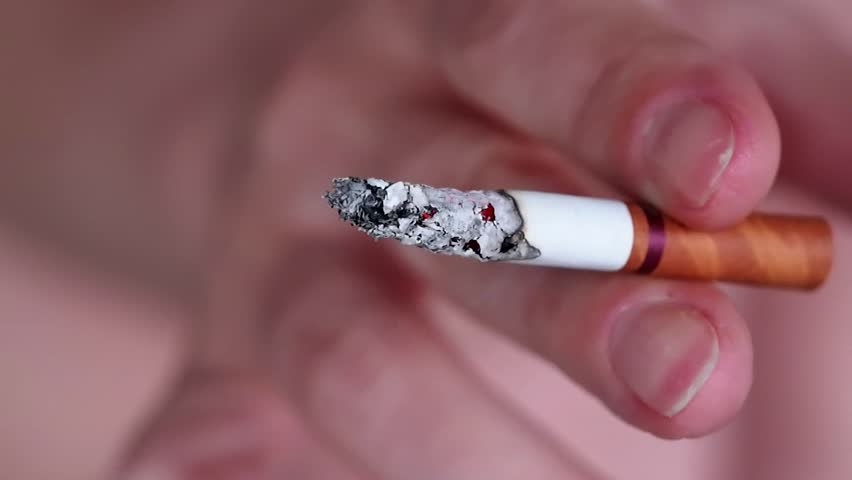 Closeup on a burning cigarette being hold by a woman