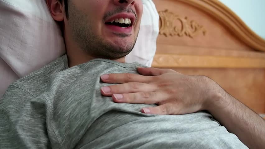 Young man in pain in his bed. His hand is touching his chest.