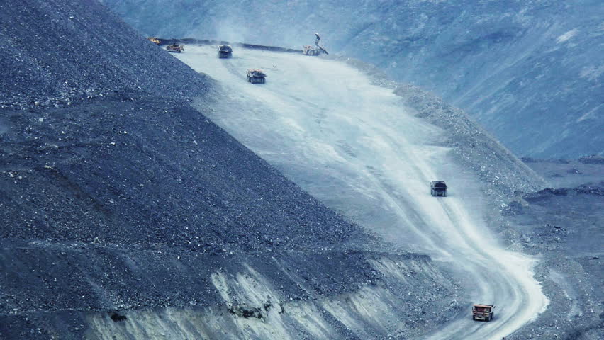 Heavy mining dump trucks moving along the opencast, far