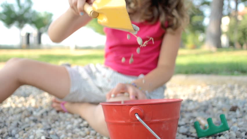 Slow Motion Shot Of A Small Stones Falling From Spade To Bucket. Girl Playing In