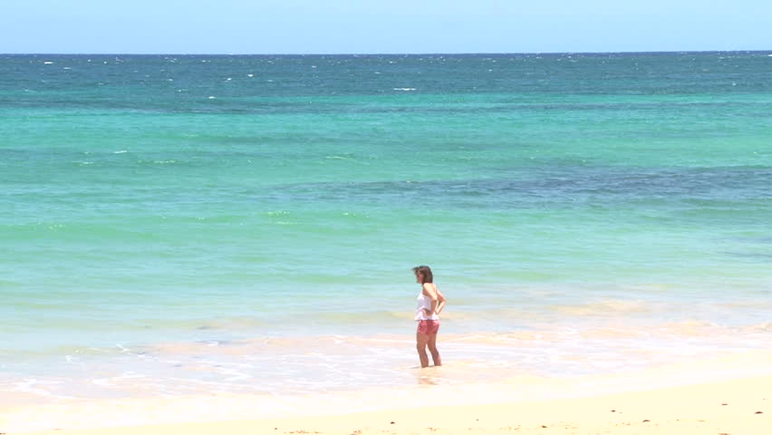 Model released woman walking on sandy beach on beautiful, blue sky day in