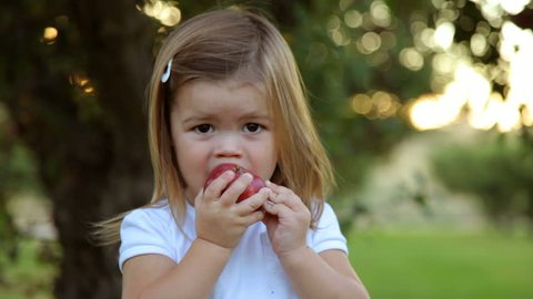 Young girl in orchard take bite of apple