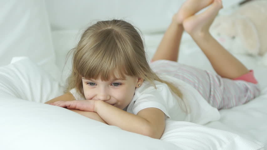 Funny little girl lying in bed smiling and laughing