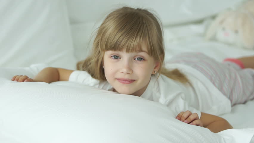 Cute little girl lying in bed and smiling at camera
