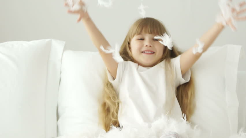 Funny little girl playing with pillow feathers and laughing