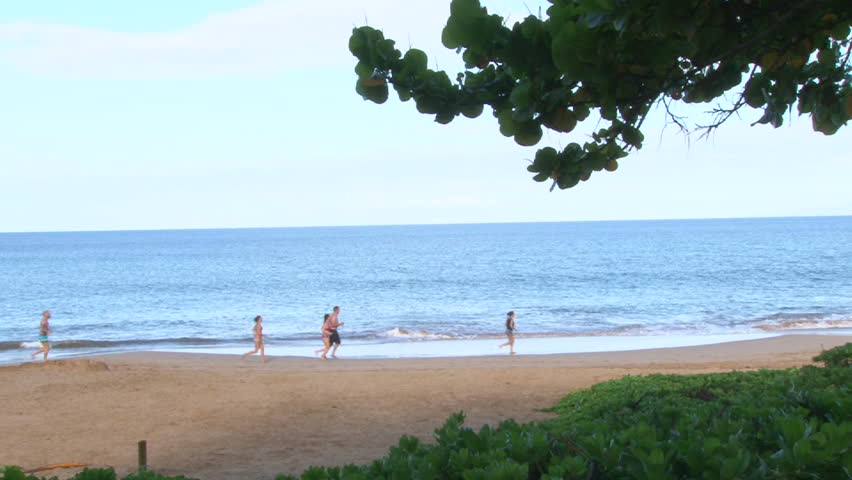 Men and women running on sandy beach.