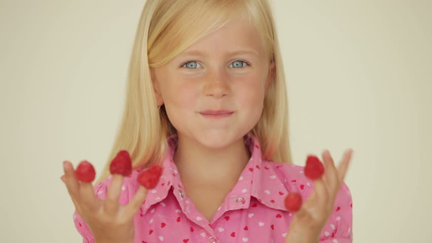 Beautiful little girl eating raspberries from top of her fingers and smiling