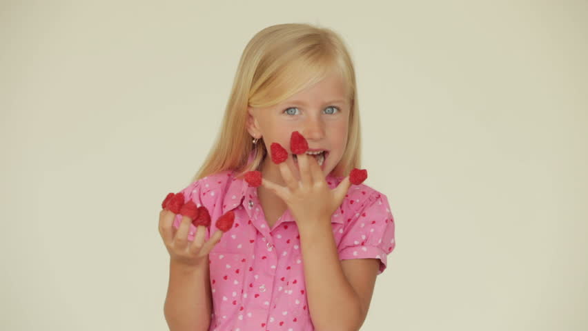Cute little girl eating raspberries from top of her fingers and smiling