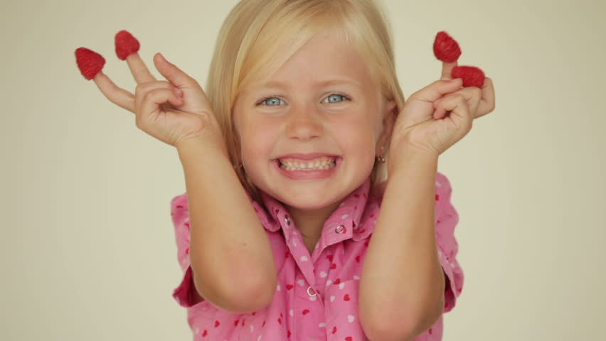 Adorable little girl eating raspberries from top of her fingers and smiling