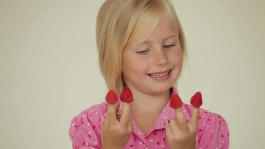Cheerful little girl eating raspberries from top of her fingers and smiling